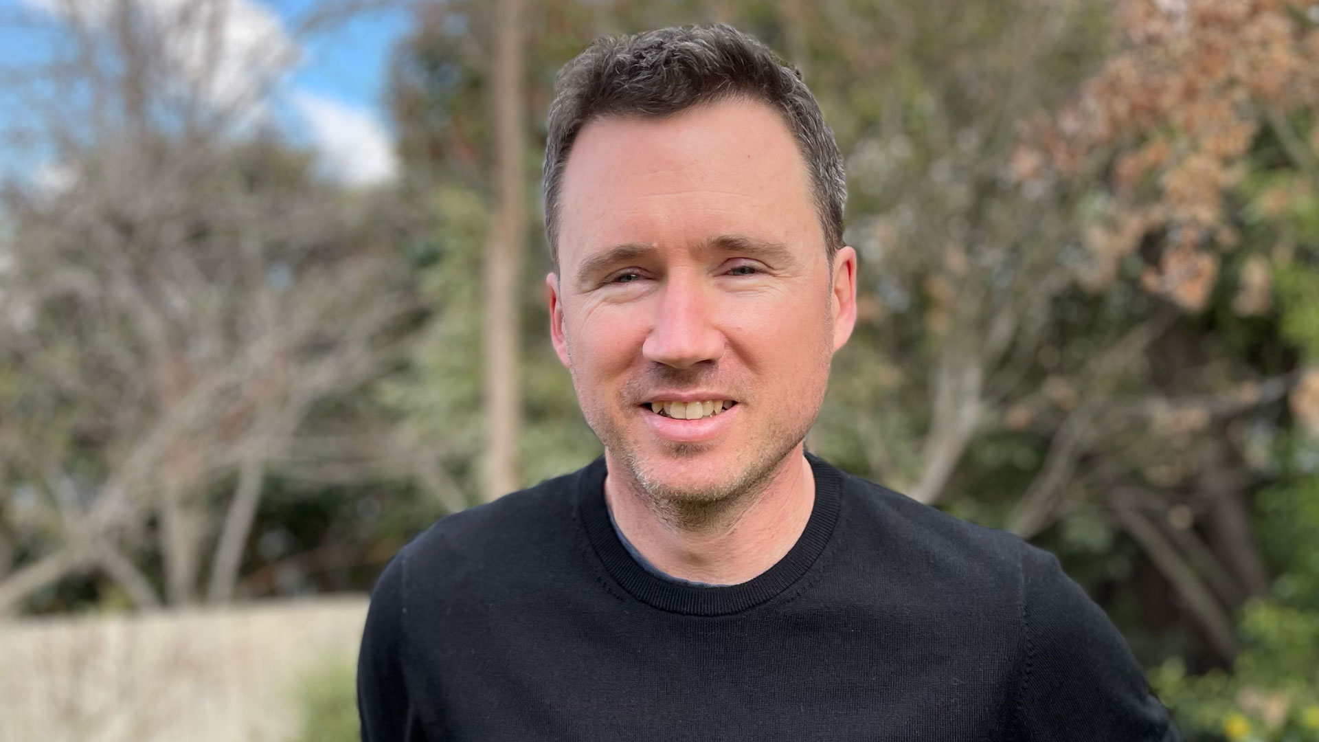Photo of Brett Matson wearing a black jumper and standing in a garden. Next to him is the text: "People are capable of much more than their current role description and they just need an opportunity to try".