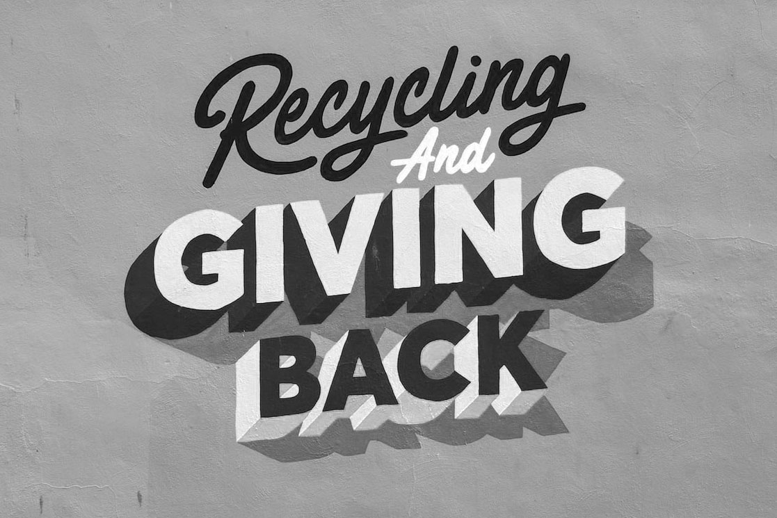 Photo of a plain wall with the words "Recycling and giving back" painted on it.