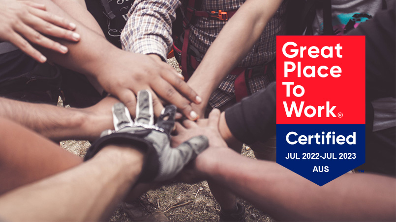 Close up photo of lots of people's hands all place together in a circle. Some are wearing work gloves. You can't see any faces. Above the photo is a crest saying that Sitback is Great Place To Work certified.