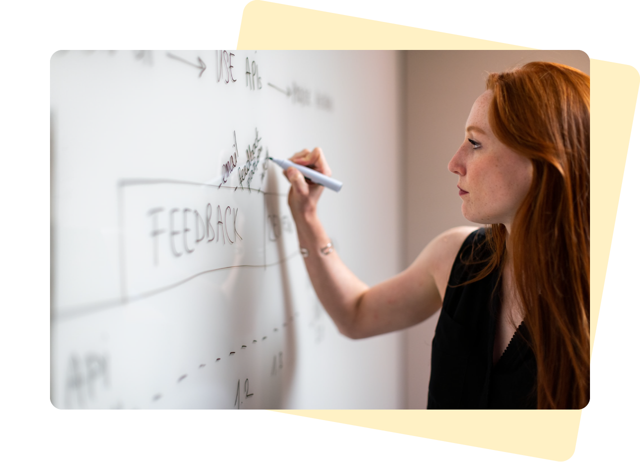 Customer research - Photograph of a caucasian woman with long auburn hair and a black sleeveless top writing on a whiteboard