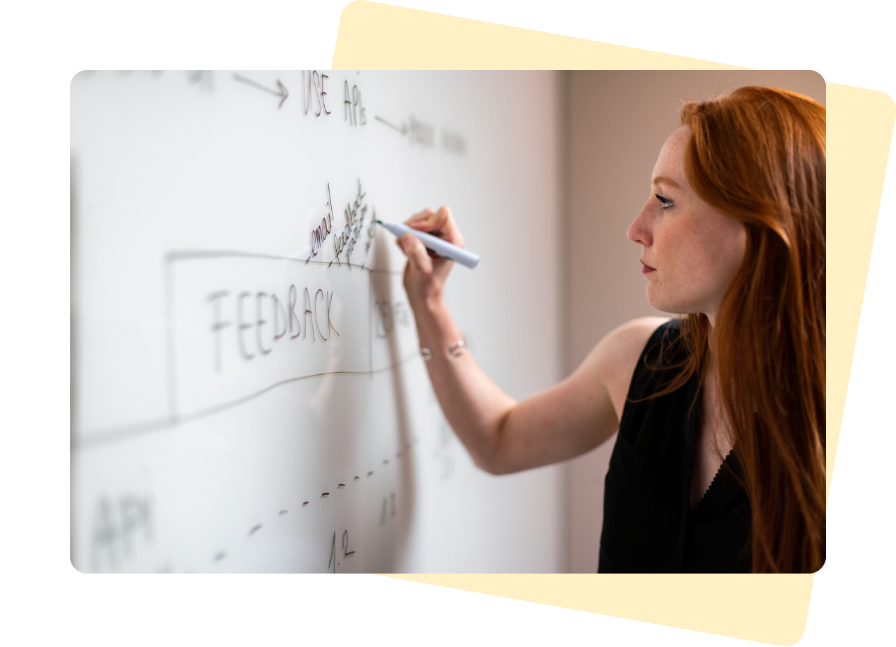 Customer research - Photograph of a caucasian woman with long auburn hair and a black sleeveless top writing on a whiteboard