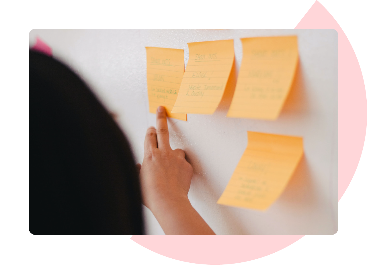 Experience design - photo of a woman's hand pointing at an orange post-it note stuck on a whiteboard. The detail is obscured.