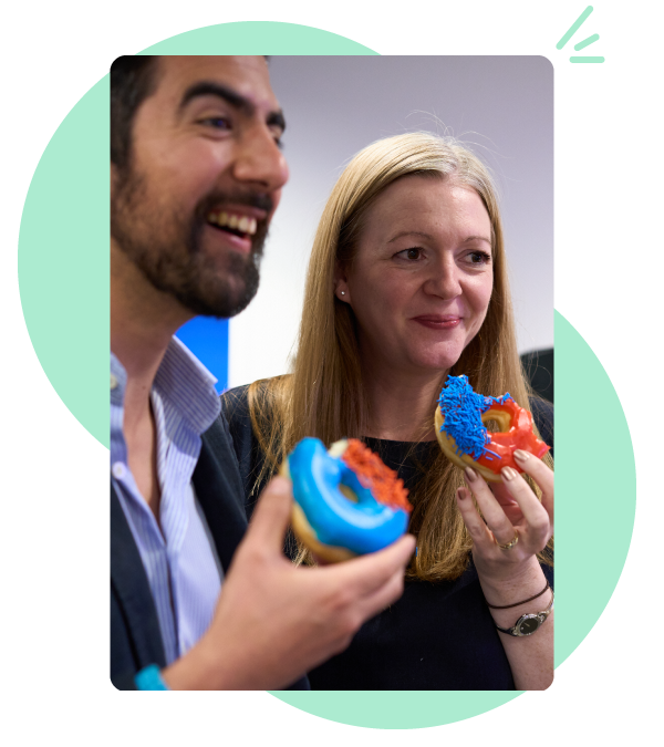 Close up photo of a man and a woman laughing while eating donuts with brightly coloured icing on top.