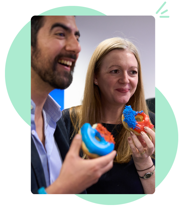 Close up photo of a man and a woman laughing while eating donuts with brightly coloured icing on top.