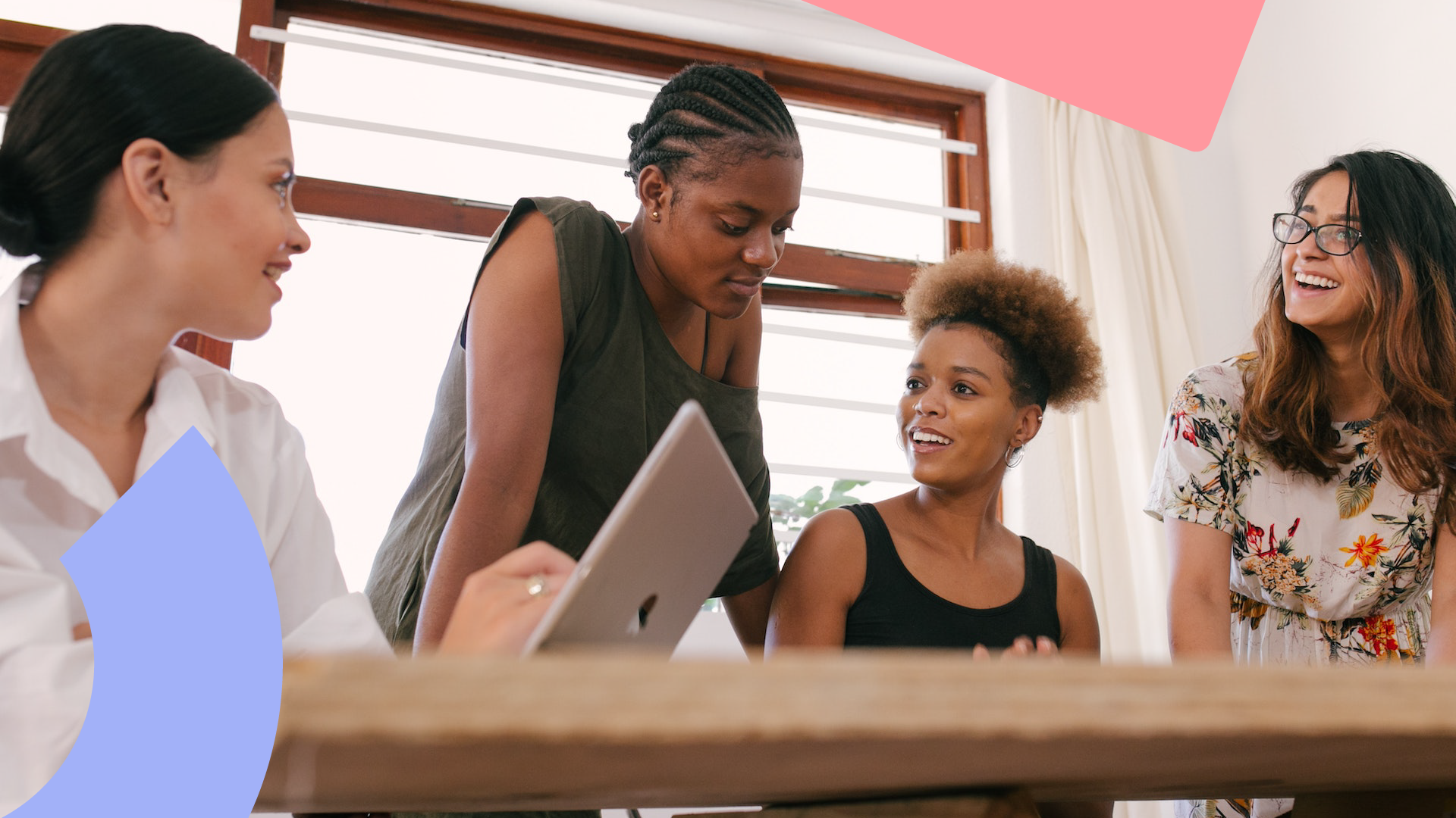 A group of 4 women sat around a table in their workplace discussing something.