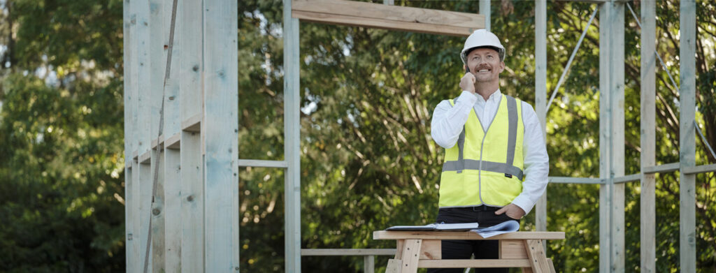 Construction site worker wearing a hi-vis jacket and hard hat while using a mobile phone.