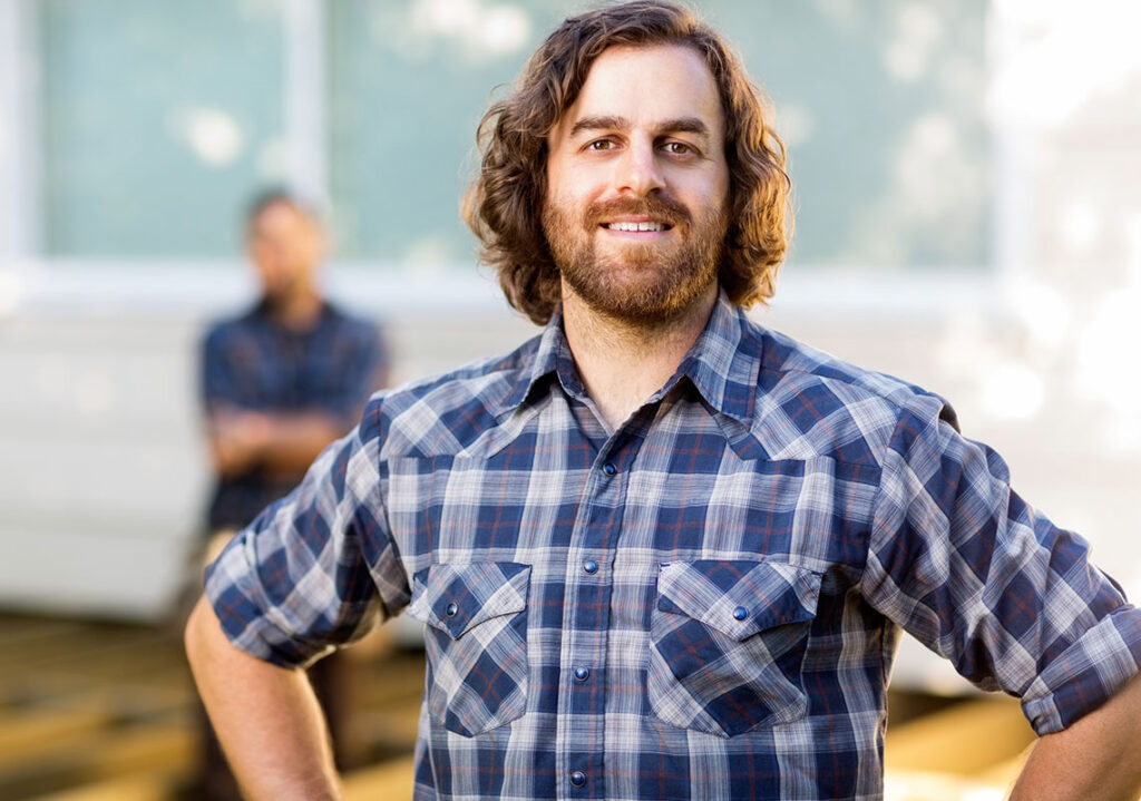 Small business owner - Man with long hair and a short beard, wearing a plaid shirt.
