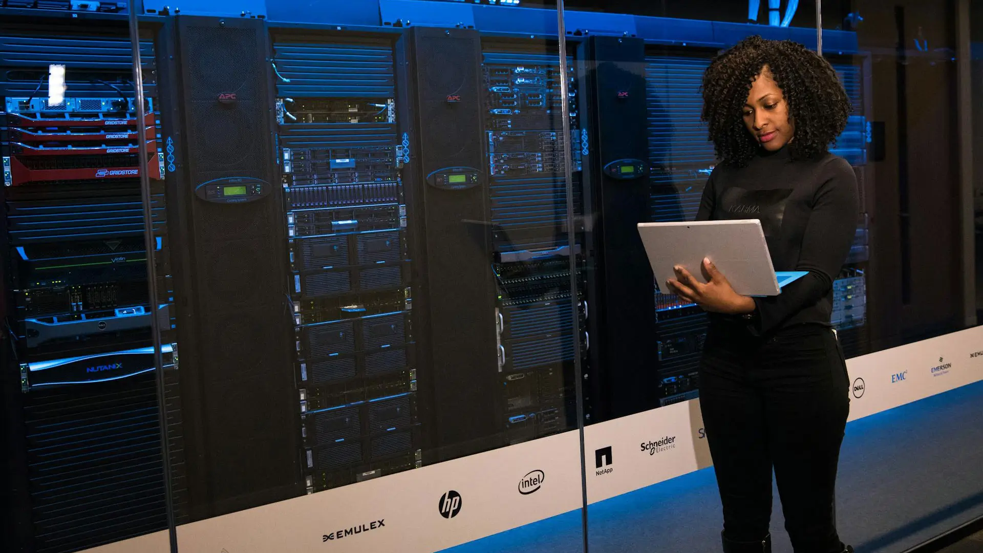 Woman using a laptop standing in front of a data centre server rack.