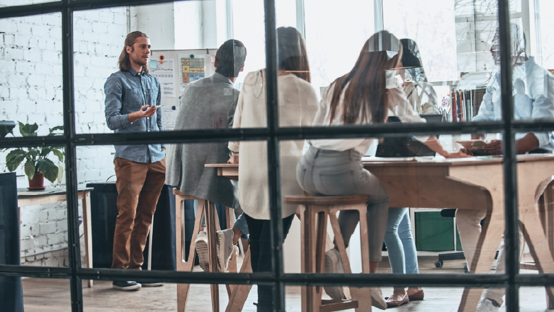 Room full of people having a meeting, photographed through window glass.