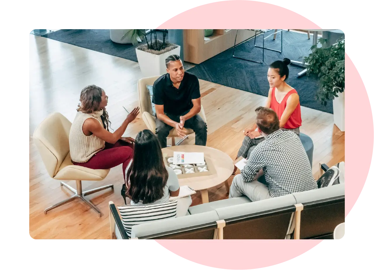 Diverse team in a casual group discussion, seated in a modern workspace around a circular table.