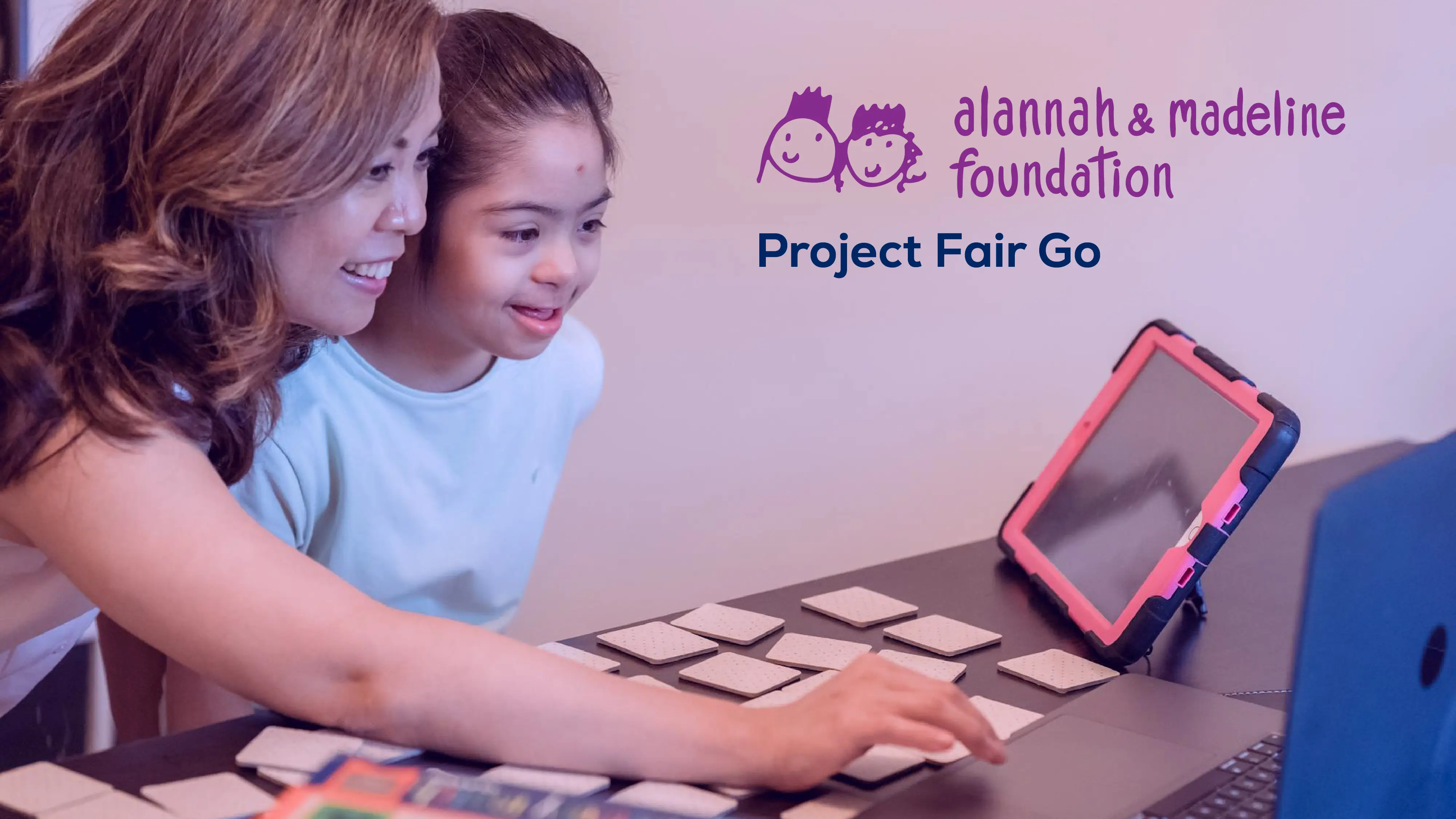 A female educator is showing a child with special needs how to use a laptop. The Alannah & Madeline logo - Project Fair Go.